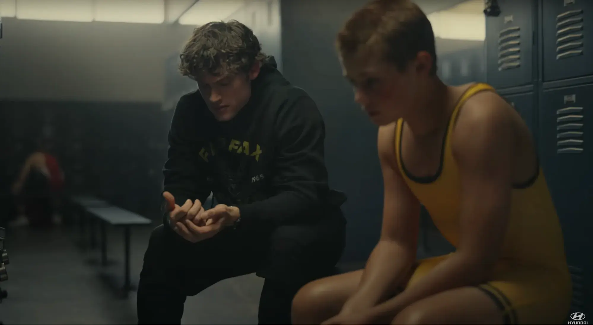 Screen cap from the ad. A 20-something guy sits next to a small boy in wrestling gear in a locker room having a serious conversation.