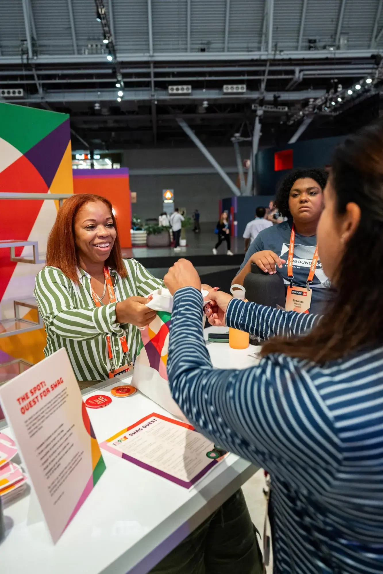 A woman working at The Spot’s INBOUND booth hands swag to a participant.