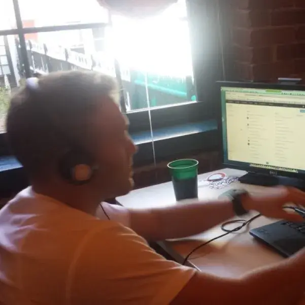 Over-the-shoulder view of a man wearing headphones and working at a computer.